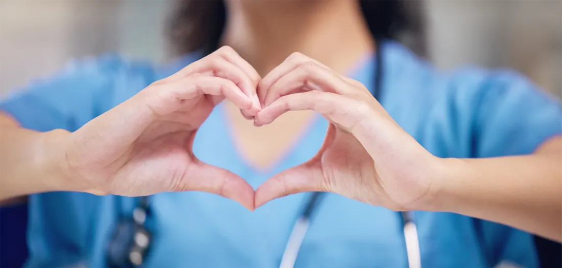 A female doctor wearing a stethoscope holding up her hands to create a heart shape
