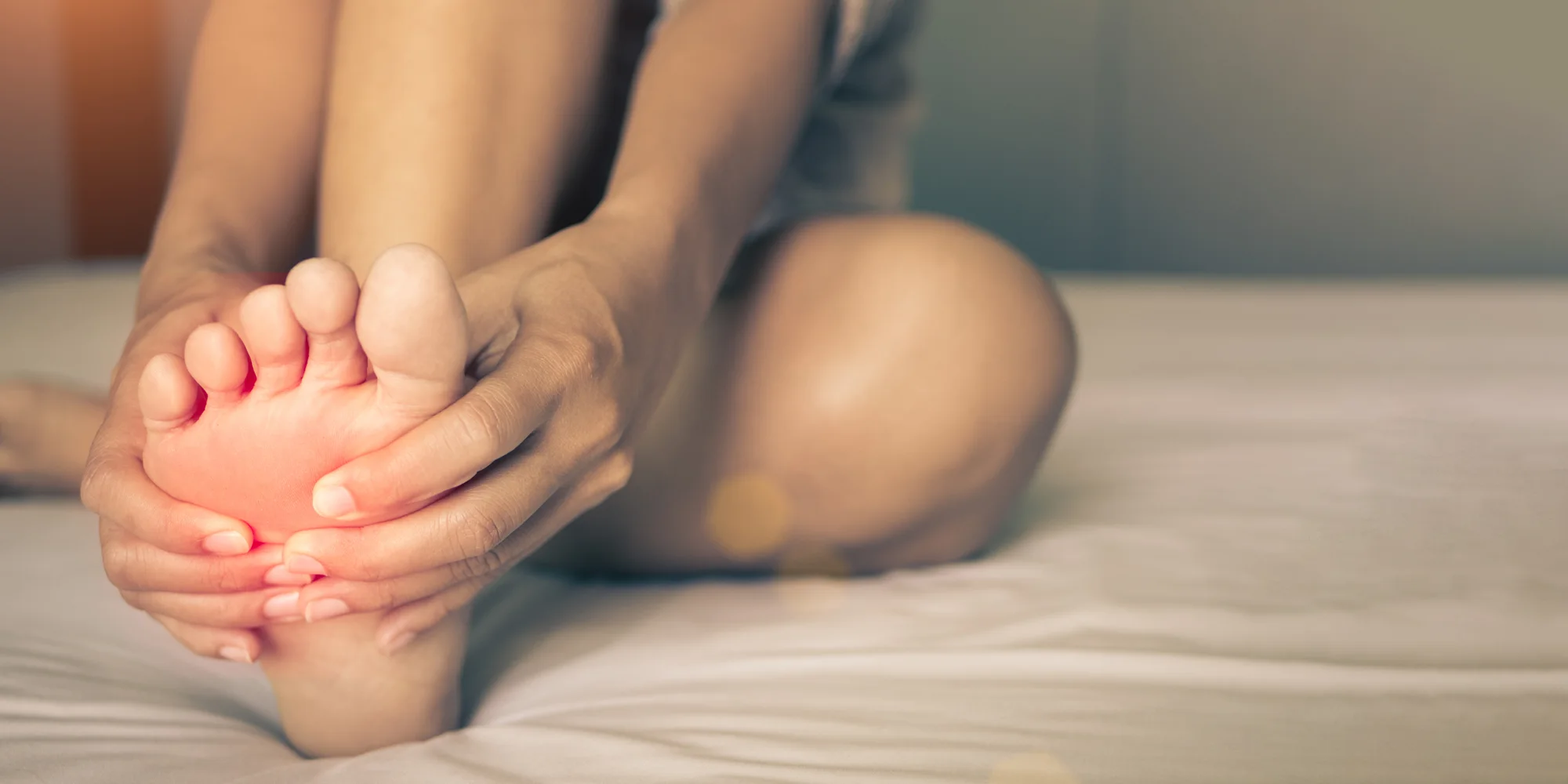 Physical Medicine Columbus GA Person With Foot Pain Person With Foot Pain sitting on a bed and clutching their foot