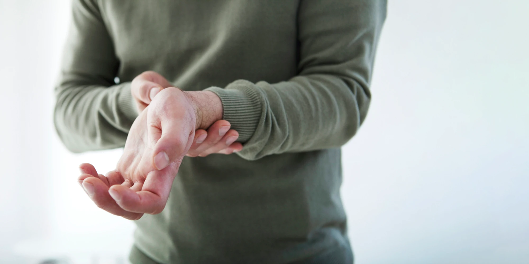Physical Medicine Columbus GA Person With Wrist Pain Person With Wrist Pain in green sweater holding their arm in pain